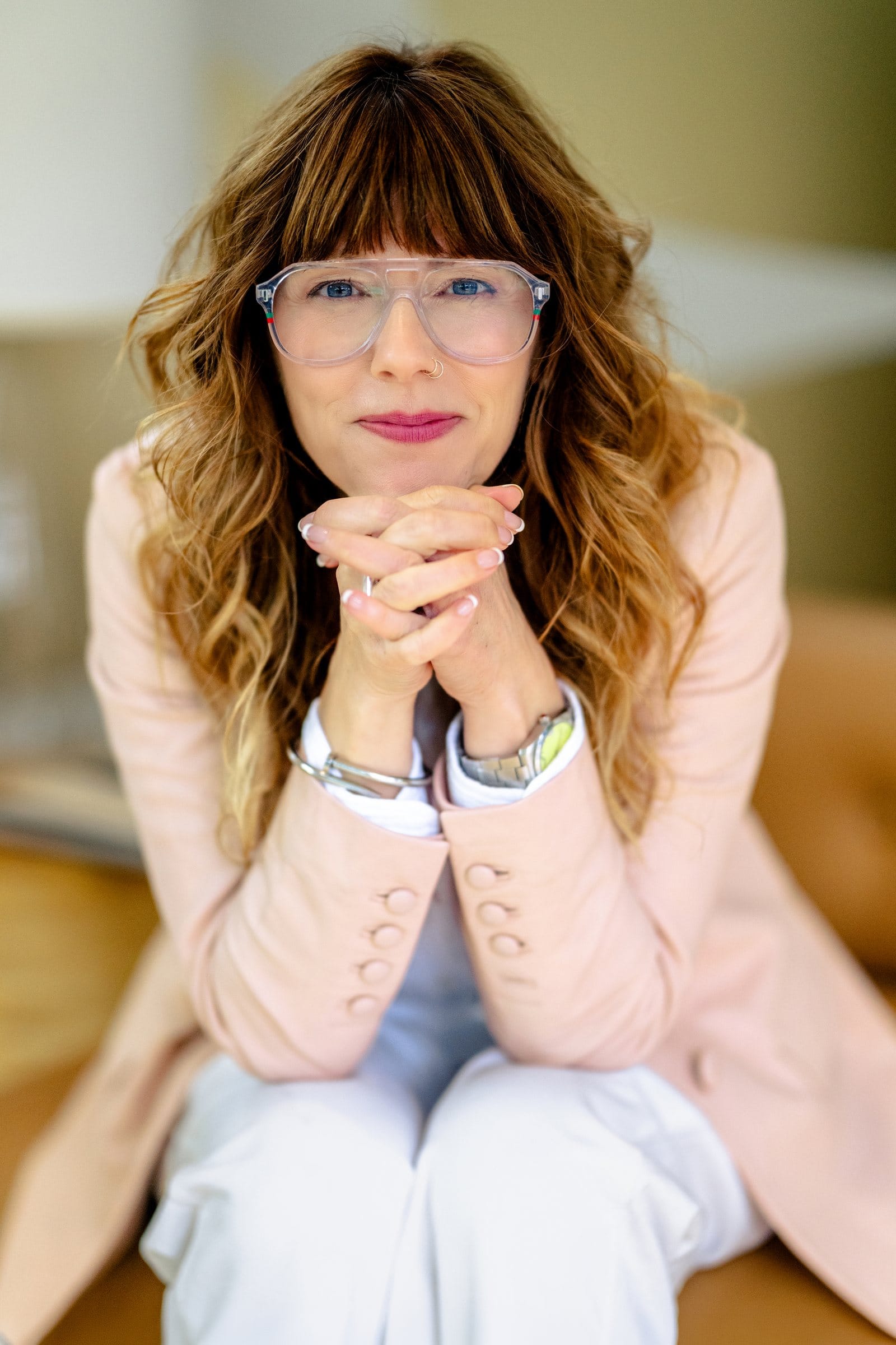 Woman in glasses with her chin on her hands, smiling softly