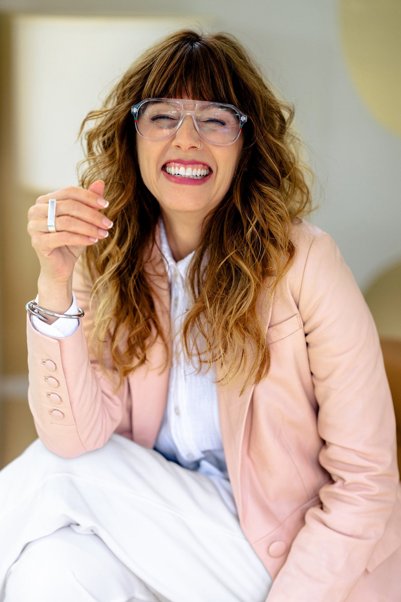 Woman in clear glasses and a pink blazer laughing