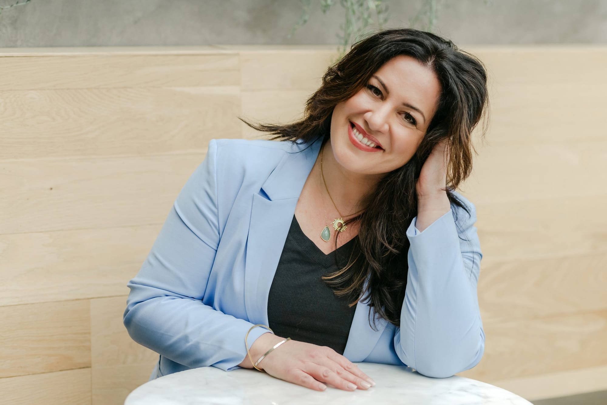 Woman in a pale blue blazer smiling at a café table