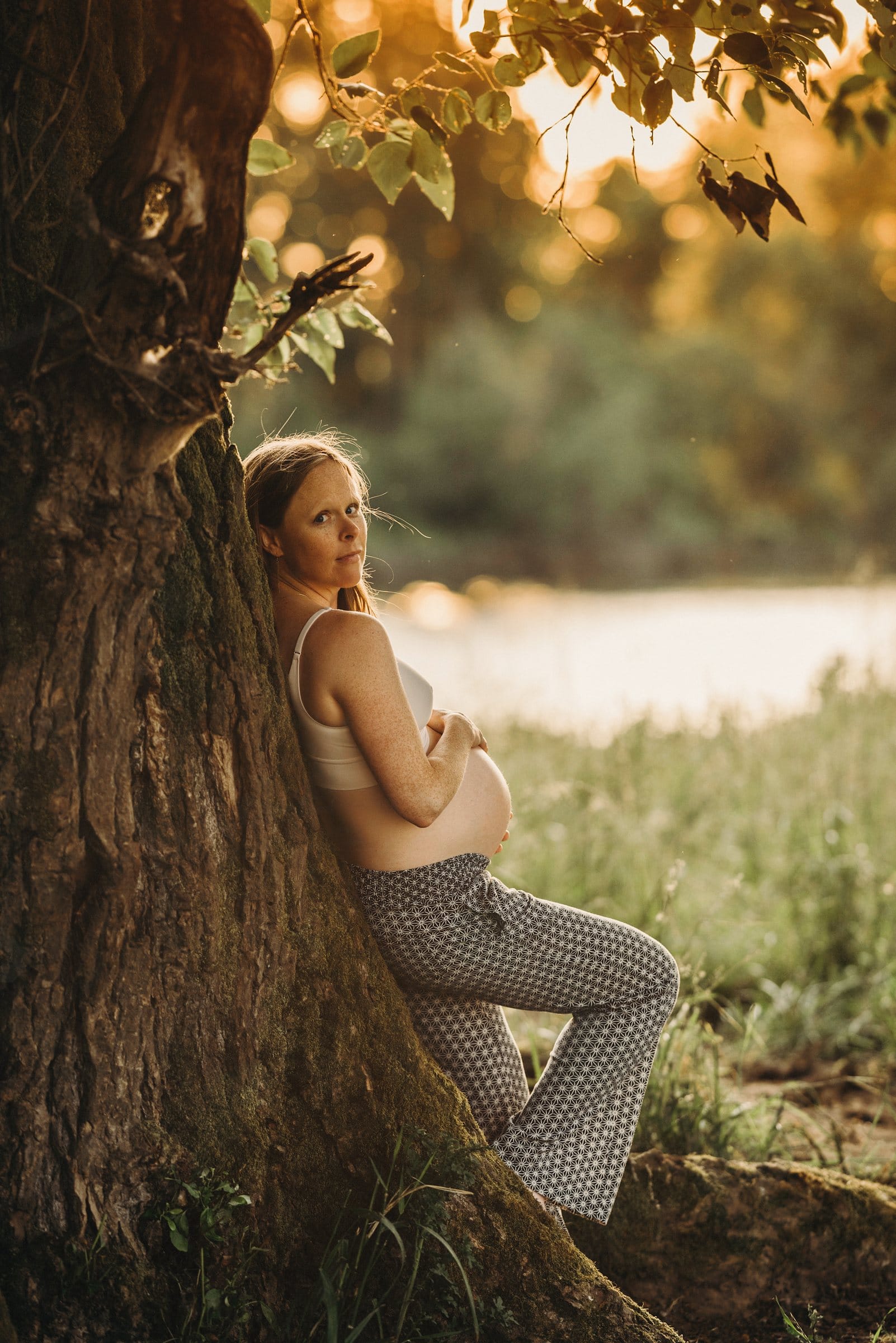 Expectant mother leaning on a tree in golden light
