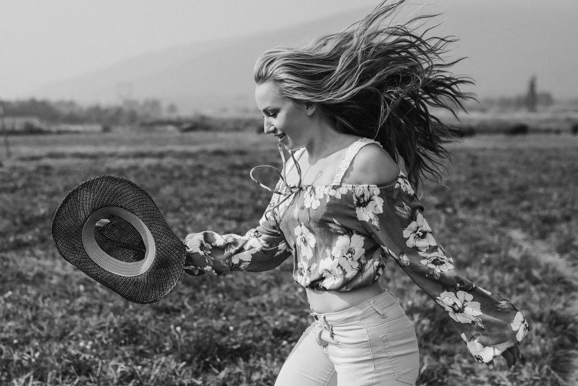 Black and white portrait of a young woman tossing her hat in a field