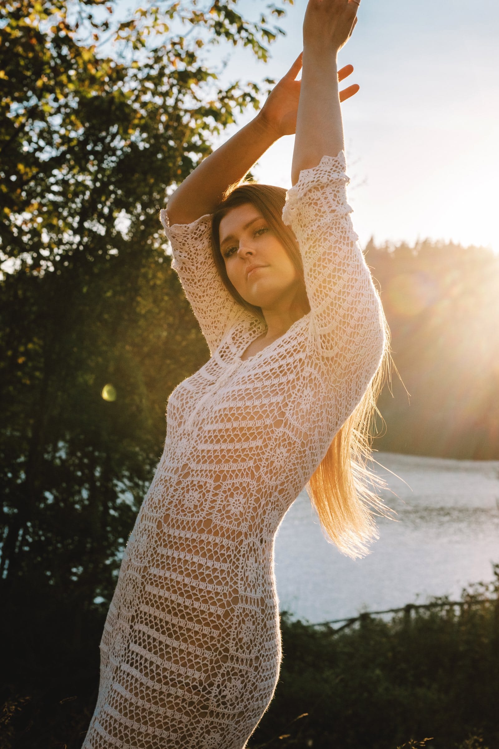 Young woman in crochet lace stretching in golden light by a lake
