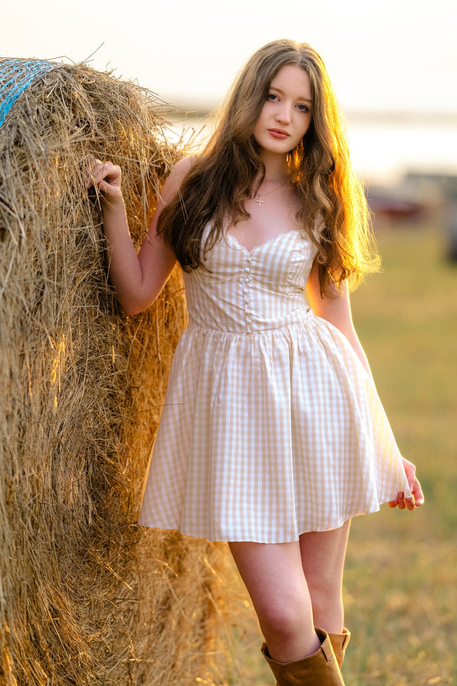 Young woman leaning on a hay bale at sunset