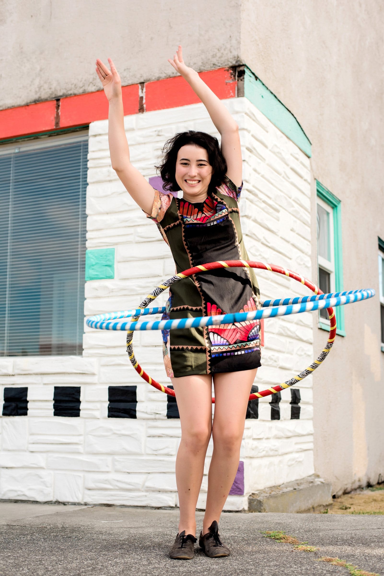 Senior girl laughing with hula hoops in front of a painted building