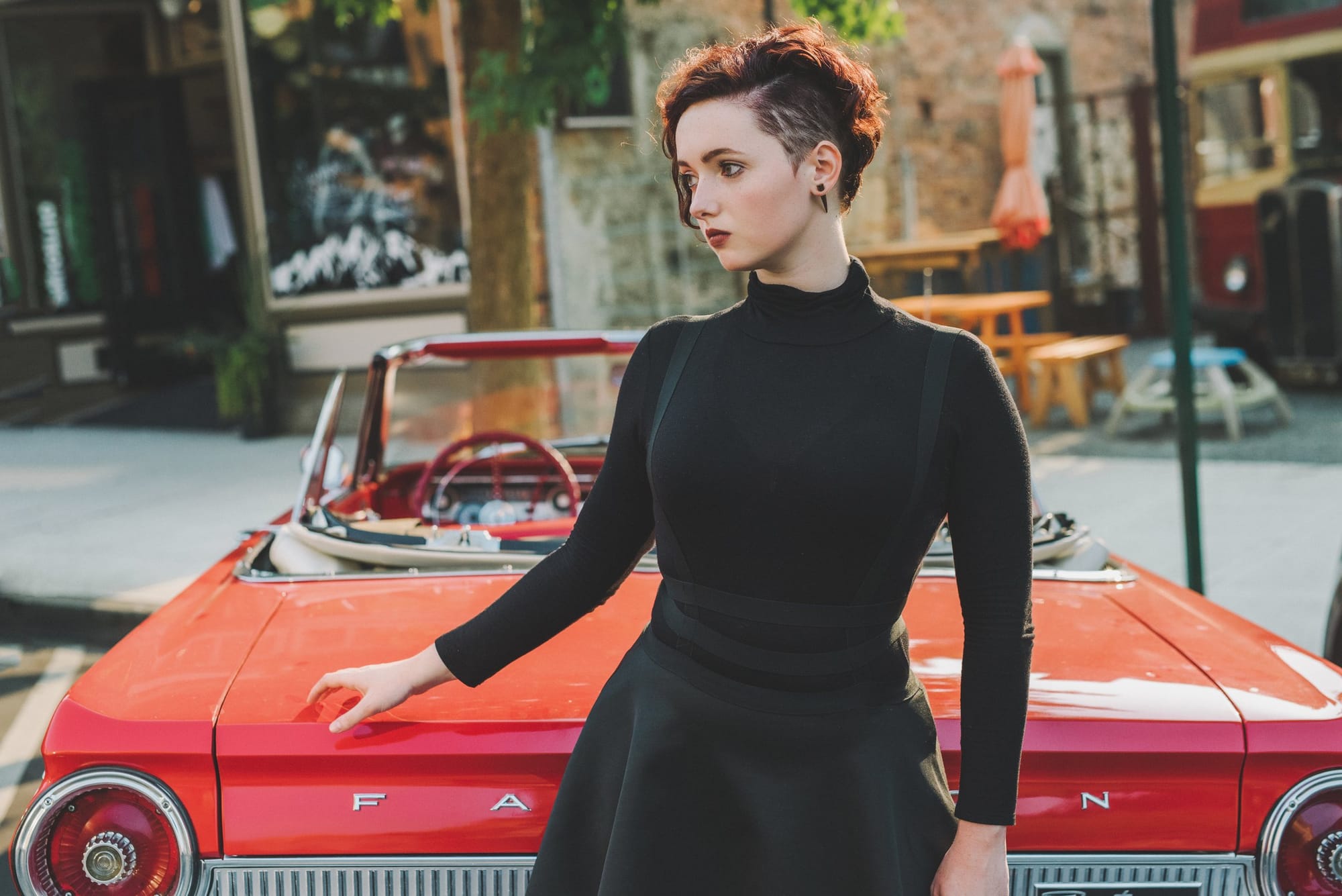 Young woman with cropped red hair leaning on a red convertible