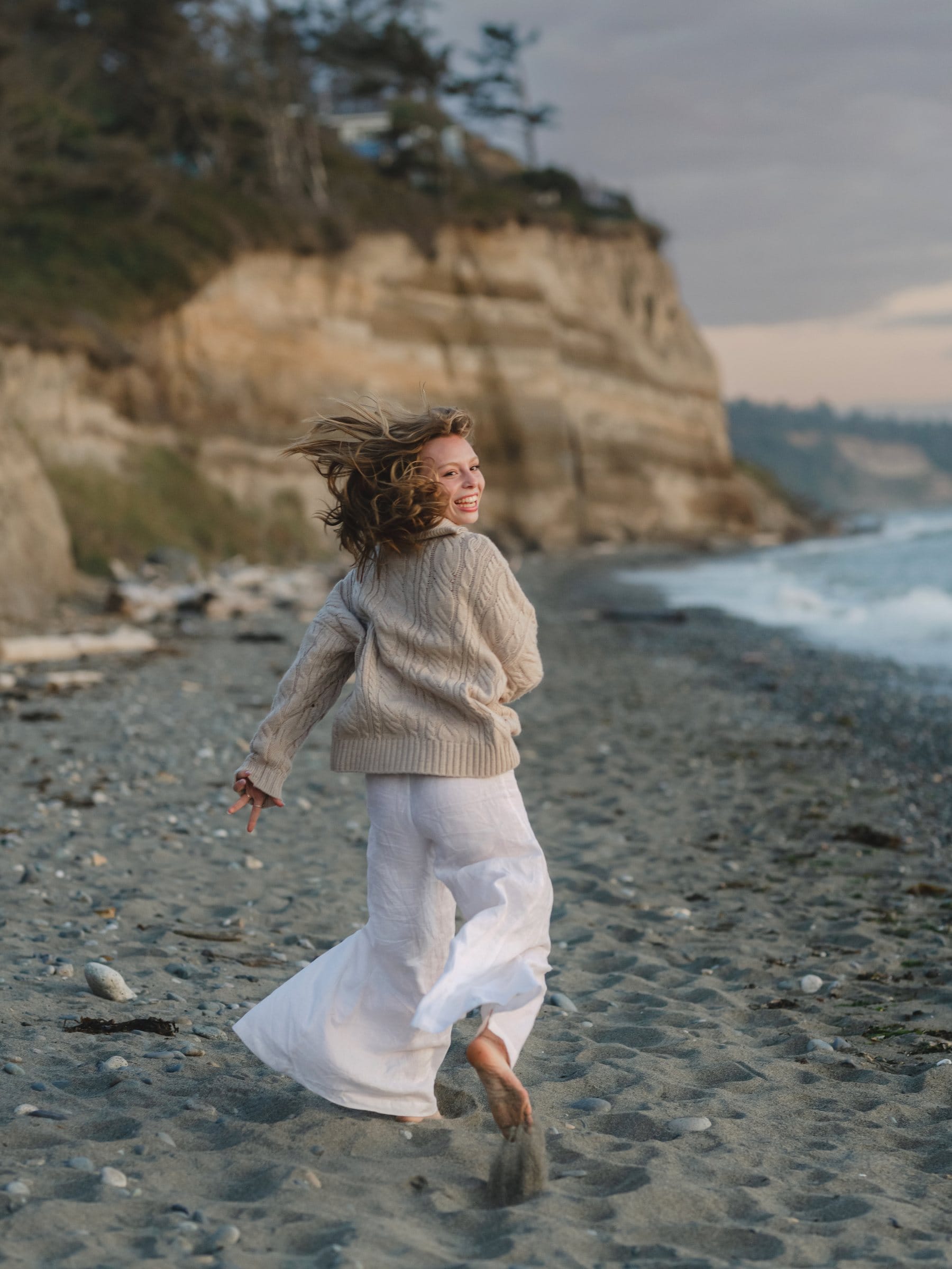 Young woman twirling on a beach below a bluff