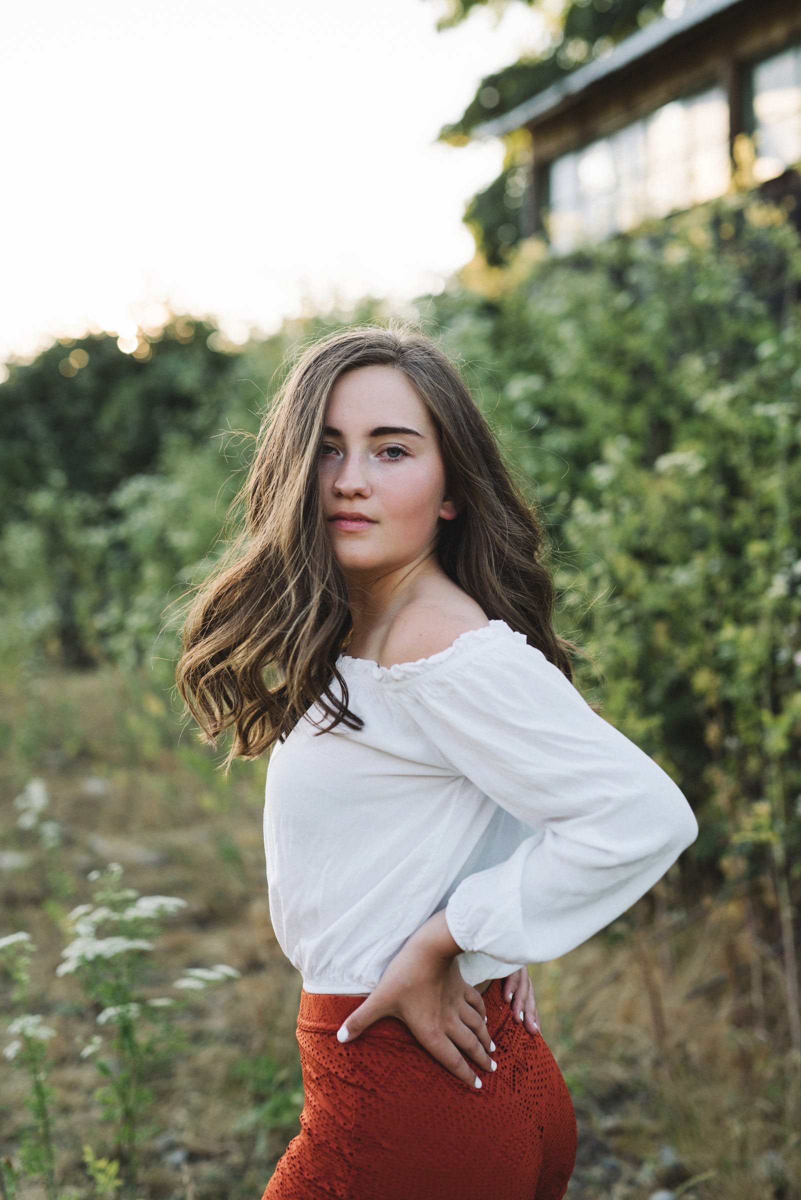 Young woman in a white blouse and rust skirt by the greenery