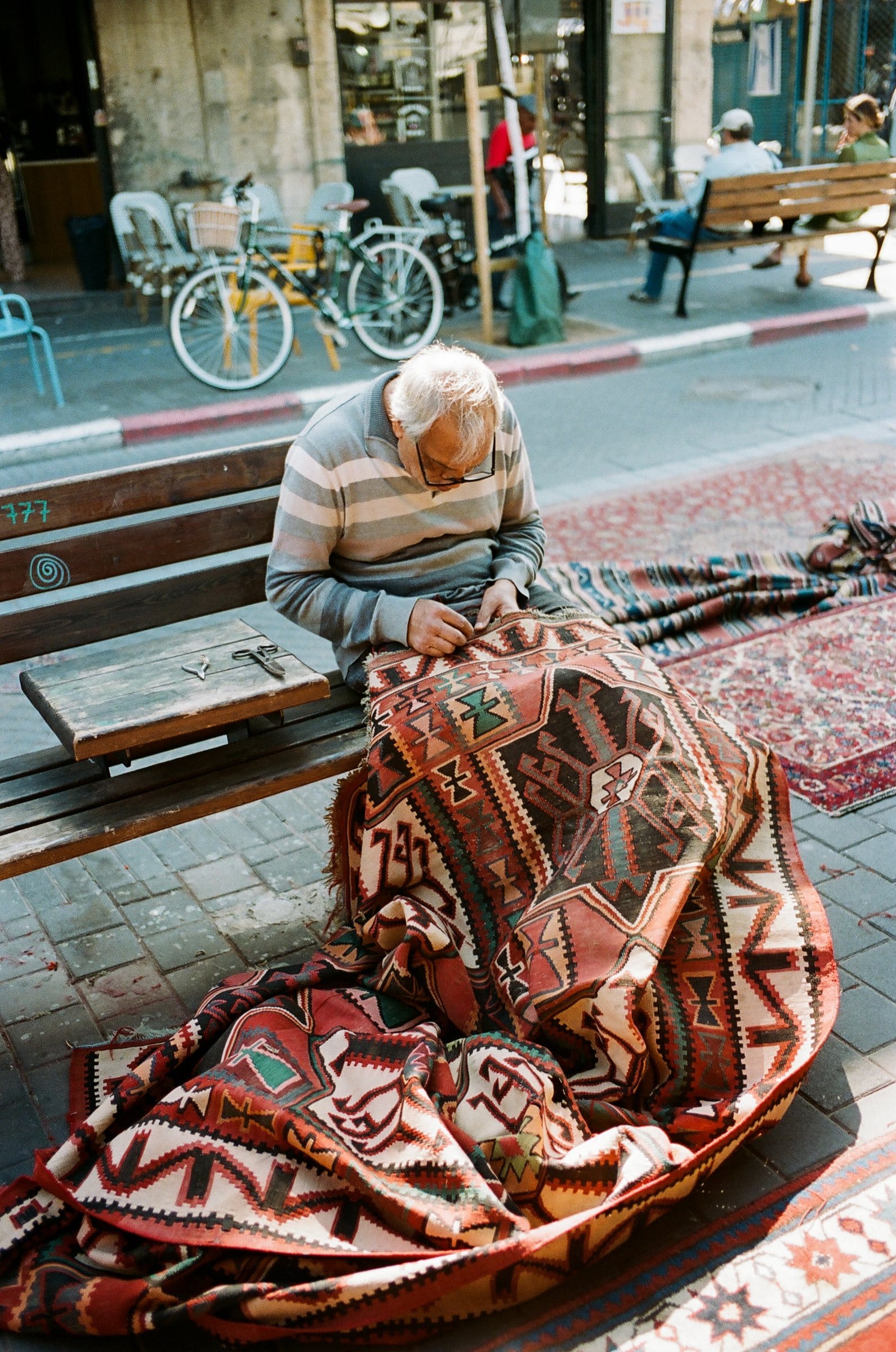 Rug seller mending a kilim on a street bench