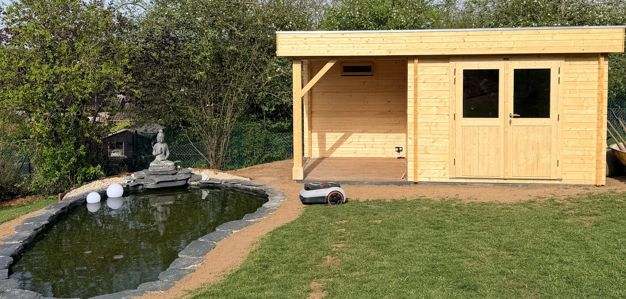 Navimow i210 LiDAR Pro en tonte autonome entre l'étang et l'abri de jardin dans un jardin du Brabant Wallon