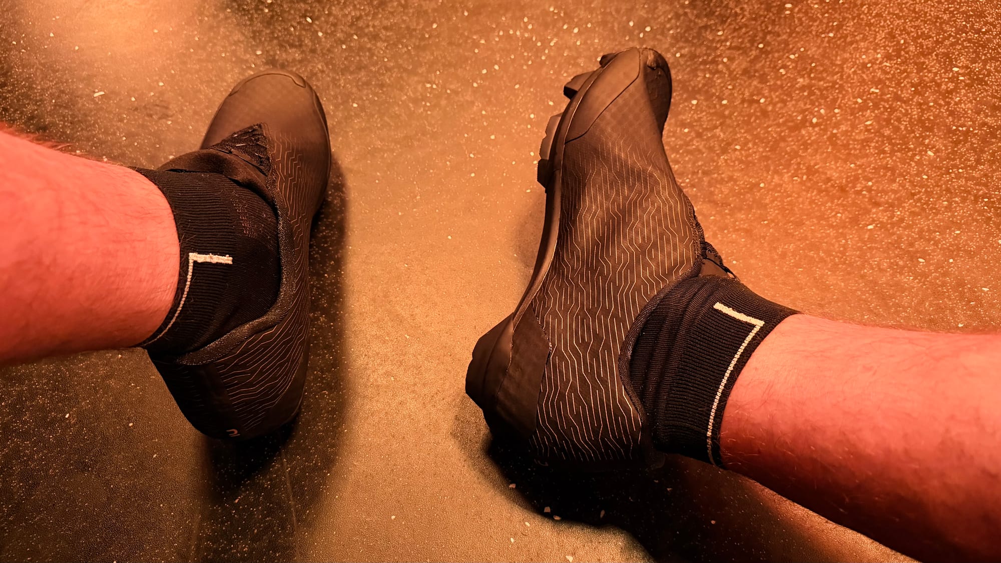 Decathlon Gravel Race 900 portées aux pieds sur les pédales d'un vélo d'indoor cycling, vue plongeante dans un studio avec éclairage rouge