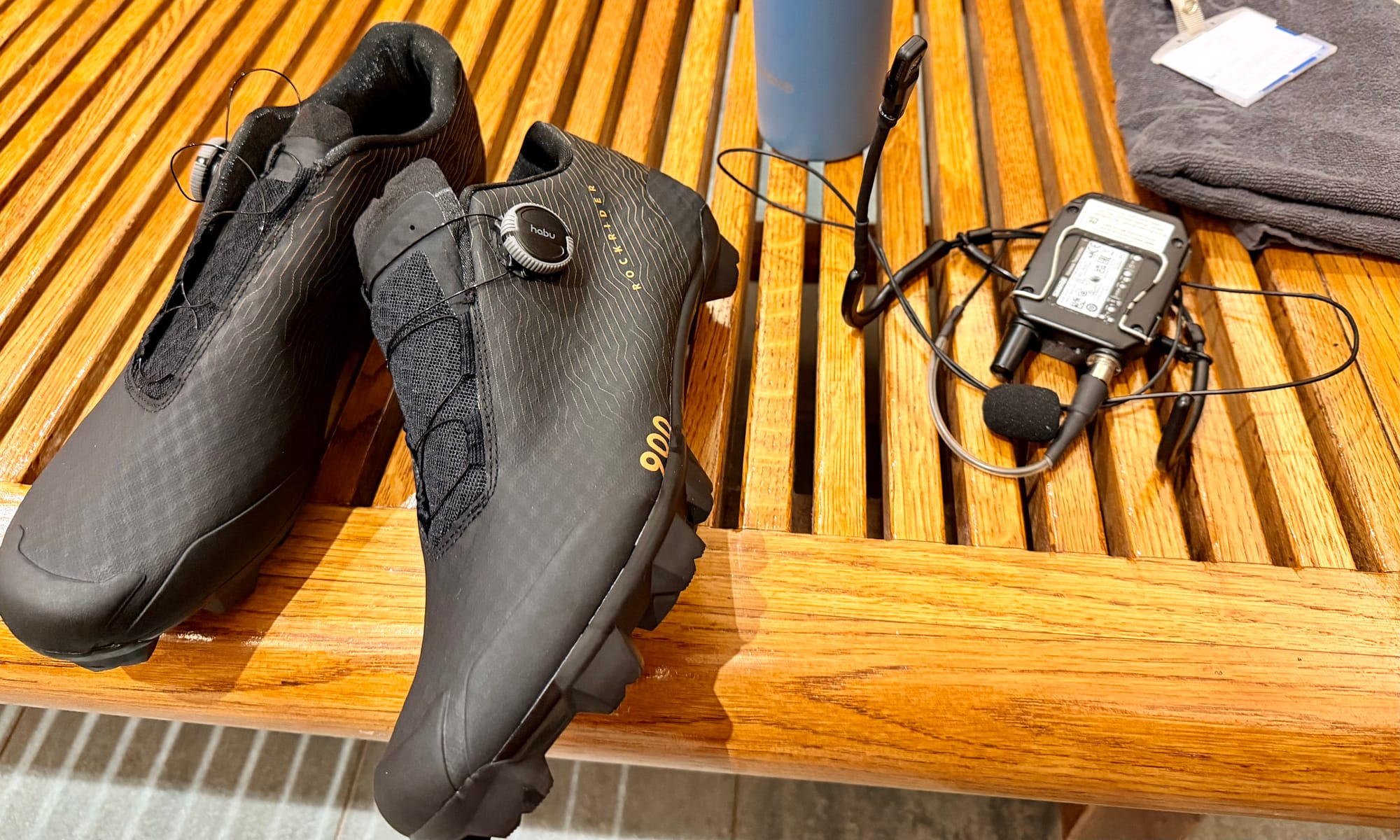 Decathlon Gravel Race 900 posées sur un banc en bois au vestiaire de l'Aspria La Rasante, à côté d'un micro-cravate et d'un émetteur