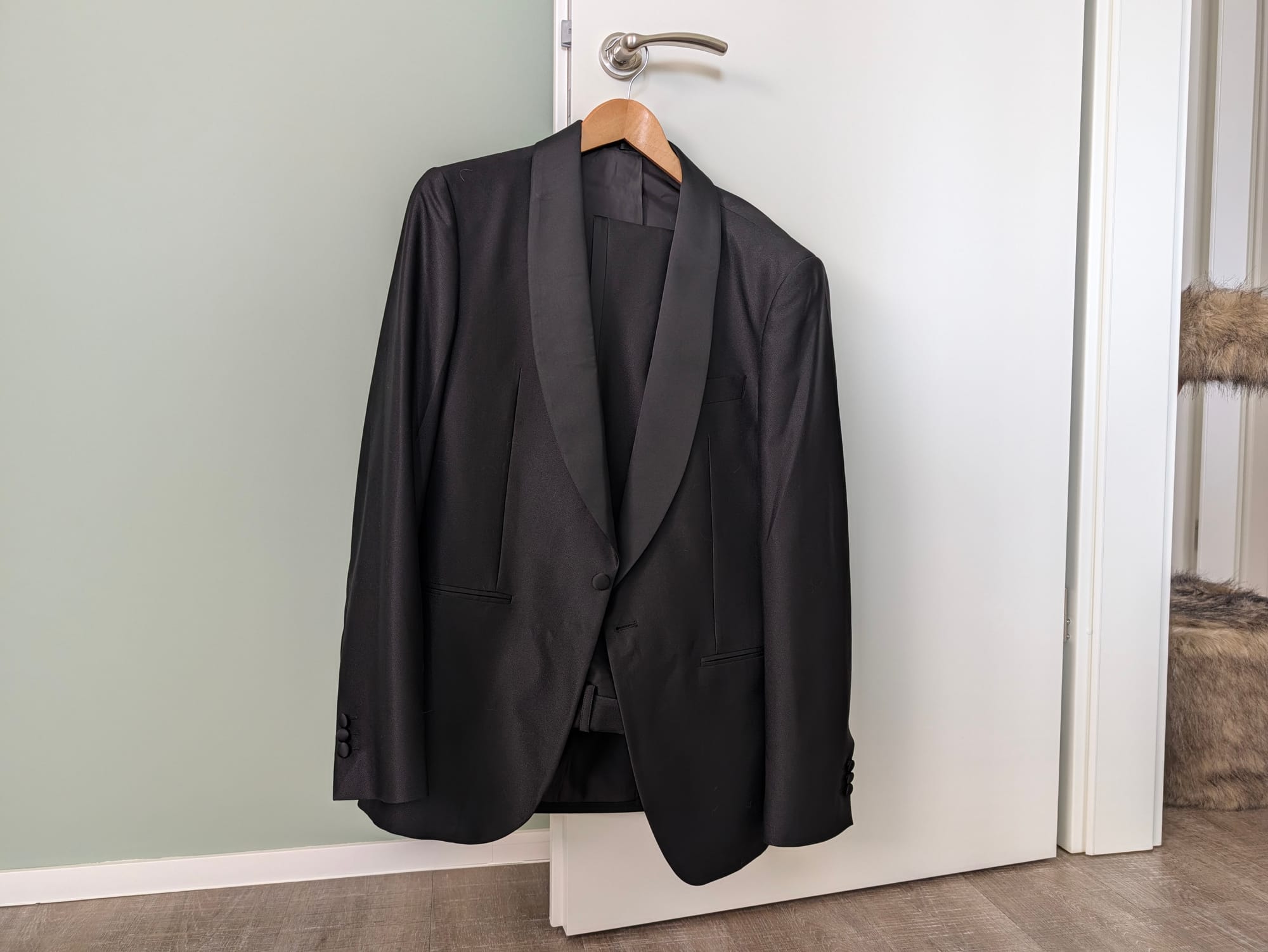 Veston de smoking noir sur mesure Hockerty avec revers châle en satin, suspendu sur une porte