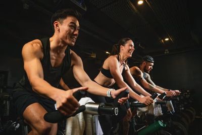 Groupe de cyclistes souriants en plein cours d'Indoor Cycling (Spinning) en salle.