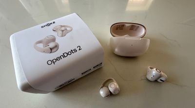 Shokz OpenDots 2 en pearl white posés à côté de leur boîte et du boîtier de charge ouvert sur un plan de travail