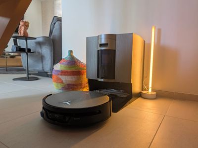 Station OmniCyclone du DEEBOT X12S en finition gris métallisé, robot noir garé devant dans un salon avec éclairage ambré