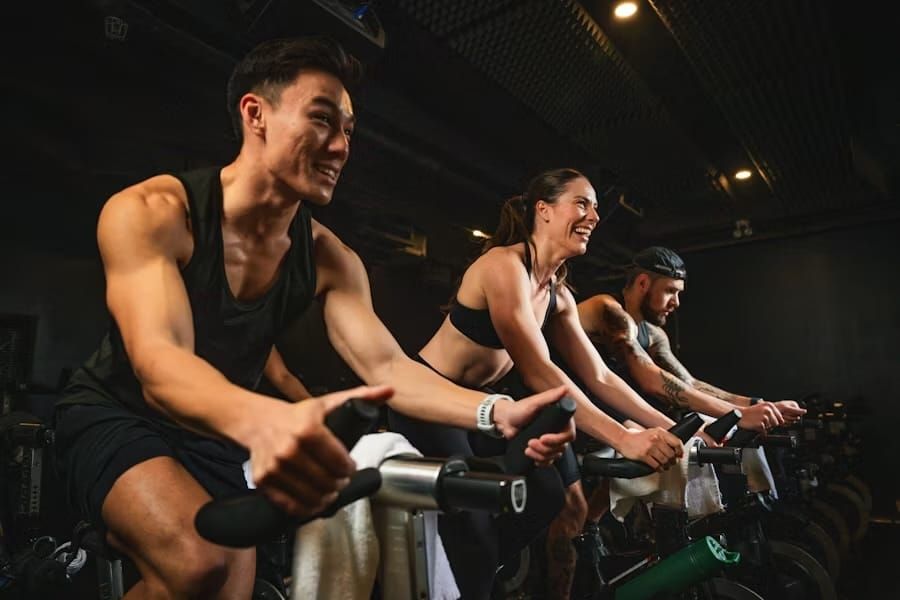 Groupe de cyclistes souriants en plein cours d'Indoor Cycling (Spinning) en salle.