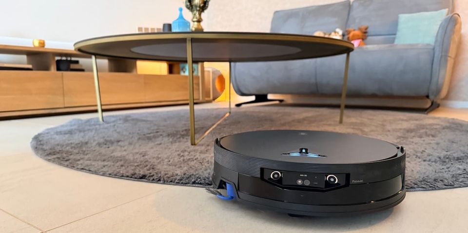 Ecovacs X12 OmniCyclone en action dans le salon entre le tapis et la table basse, capteurs FocusJet et caméra visibles à l'avant