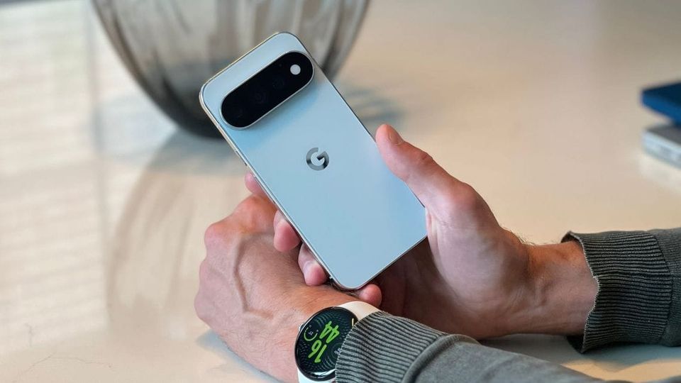 Google Pixel 11 Pro coloris Fog tenu en main, logo G et module caméra visibles, Pixel Watch 5 au poignet