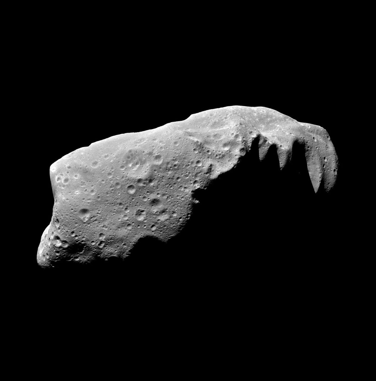 A photographic of an oblong asteroid pitted with small craters.