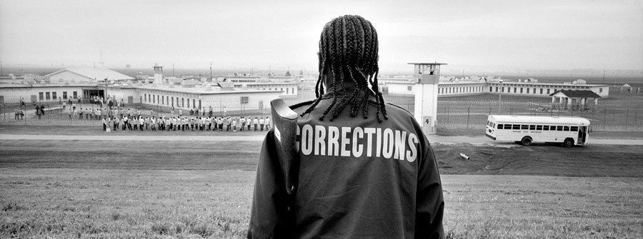A prison security guard watches from the levee as prisoners walk in lines from a prison dormitory to a pickup point.