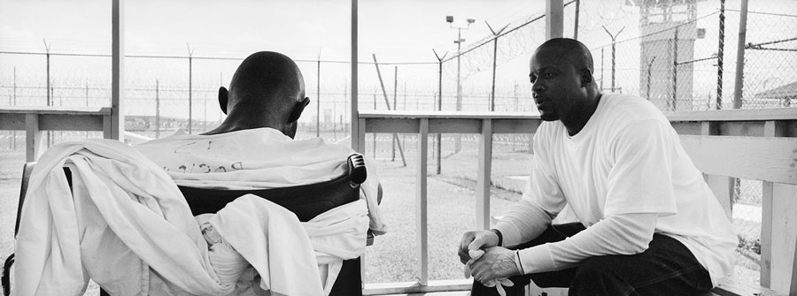 Felton Love, right, watches Timothy Minor closely in the hospital courtyard at Angola Prison. Love has volunteered to care for Minor, who is dying from a brain tumor. Minor has lost much of his muscle control. To get Minor out of his bed, Love has tied Minor to his wheel chair using sheets from his bed.