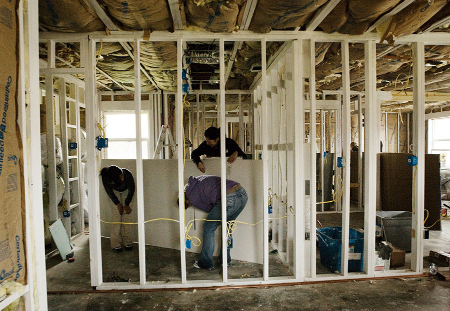 Volunteers are just starting to hang sheetrock. In any rebuild the first step is gutting. Then rotted pieces of the frame are replaced, and then the workers have to do mold remediation. The frame is cleaned and then wiped with a chemical called Shockwave. Then the house is fogged with Shockwave. The white paint on the frame is called KILZ.