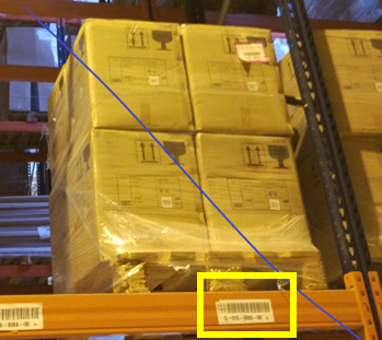 Photo of a warehouse storage location showing stacked pallets on a rack. A yellow box highlights a label with a barcode attached to the front of the rack, indicating the storage location for