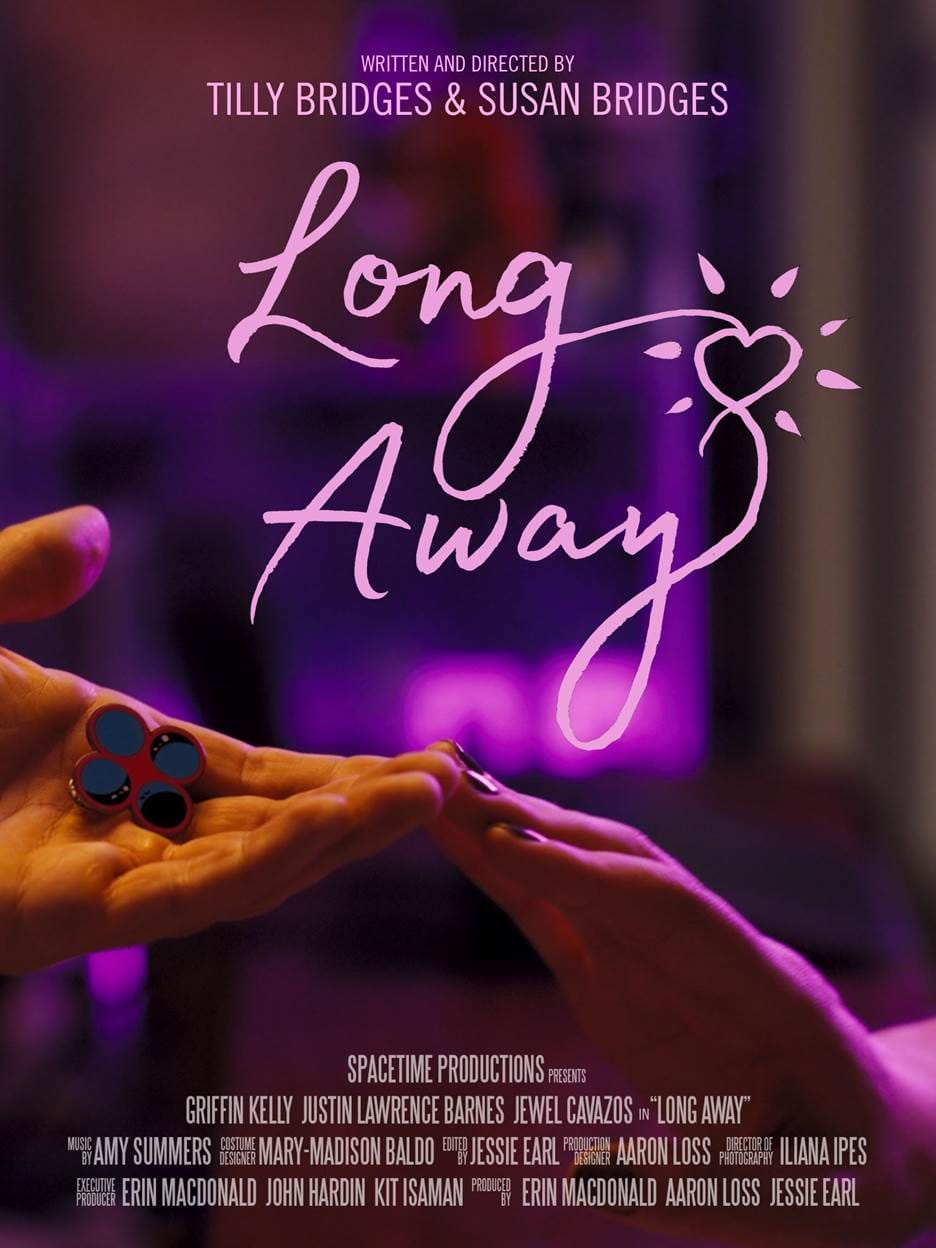 one hand reaching out, palm upward, holding an enamel pin displaying four circles, and another hand reaching out, palm downward, the two hands touch at the fingertips and are bathed in pink light. text reads: LONG AWAY WRITTEN AND DIRECTED BY TILLY BRIDGES & SUSAN BRIDGES SPACETIME PRODUCTIONS PRESENTS GRIFFIN KELLY JUSTIN LAWRENCE BARNES JEWEL CAVAZOS in “LONG AWAY” MUSIC BY AMY SUMMERS COSTUME DESIGN MARY-MADISON BALDO EDITED BY JESSIE EARL PRODUCTION DESIGNER AARON LOSS DIRECTOR OF PHOTOGRAPHY ILIANA IPES EXECUTIVE PRODUCER ERIN MACDONALD JOHN HARDIN KIT ISAMAN PRODUCED BY ERIN MACDONALD AARON LOSS JESSIE EARL