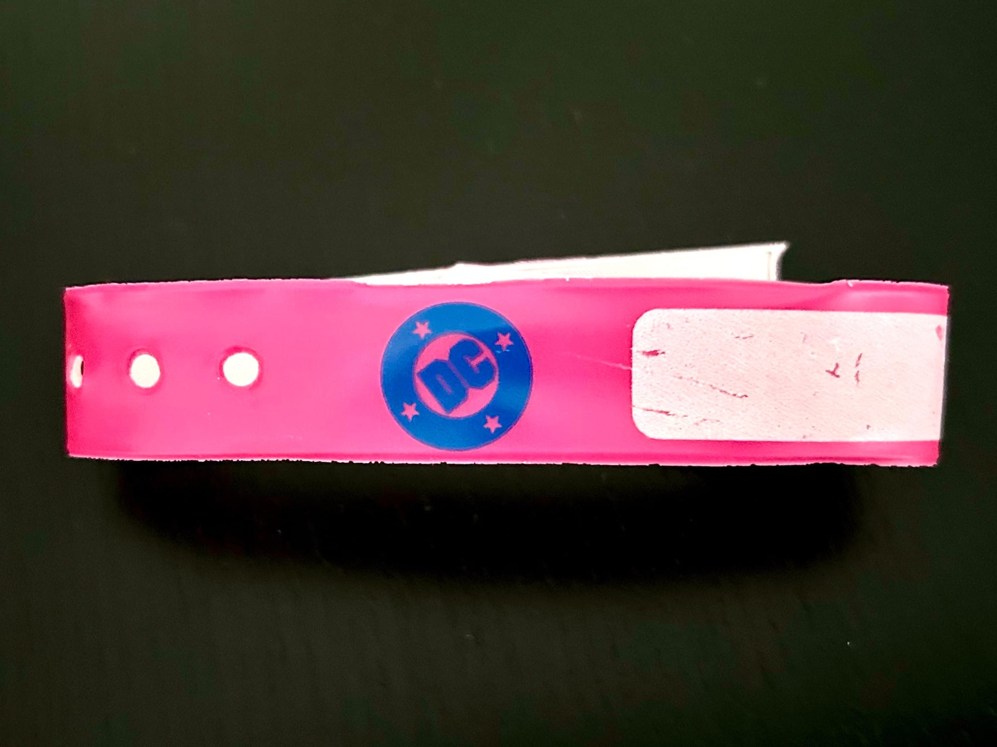 A pink temporary admittance bracelet with a blue DC bullet logo on it
