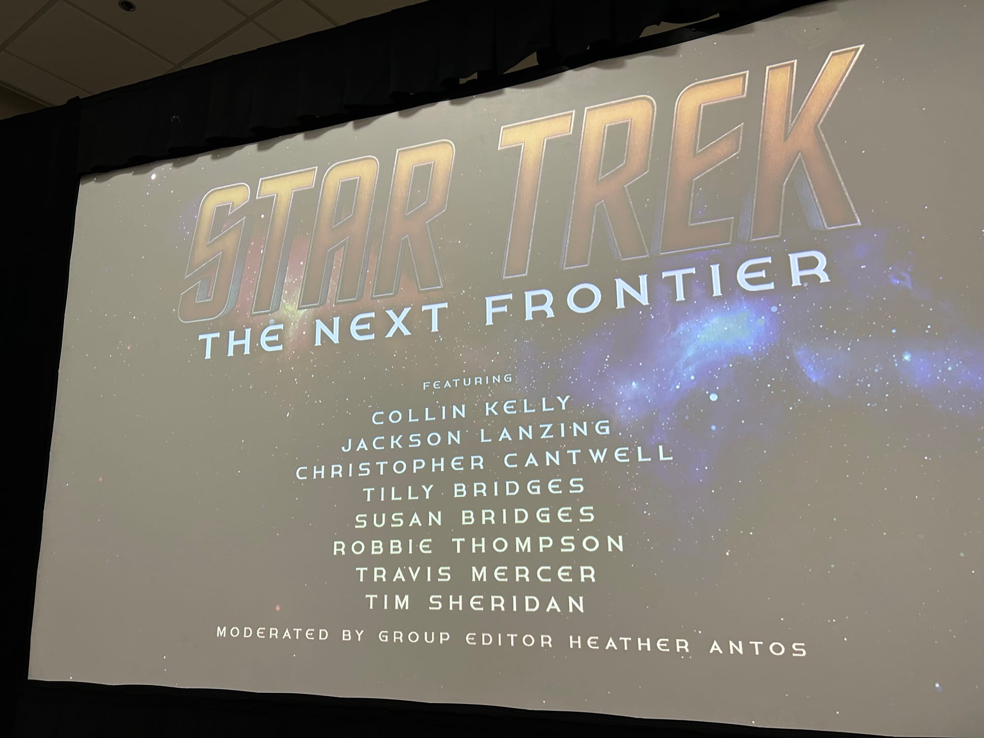 Title card on screen at the IDW Star Trek Panel at SDCC 2025, with text: Star Trek The Next Frontier featuring Collin Kelly, Jackson Lanzing, Christopher Cantwell, Tilly Bridges, Susan Bridges, Robbie Thompson, Travis Mercer, Tim Sheridan, Moderated by group editor Heather Antos