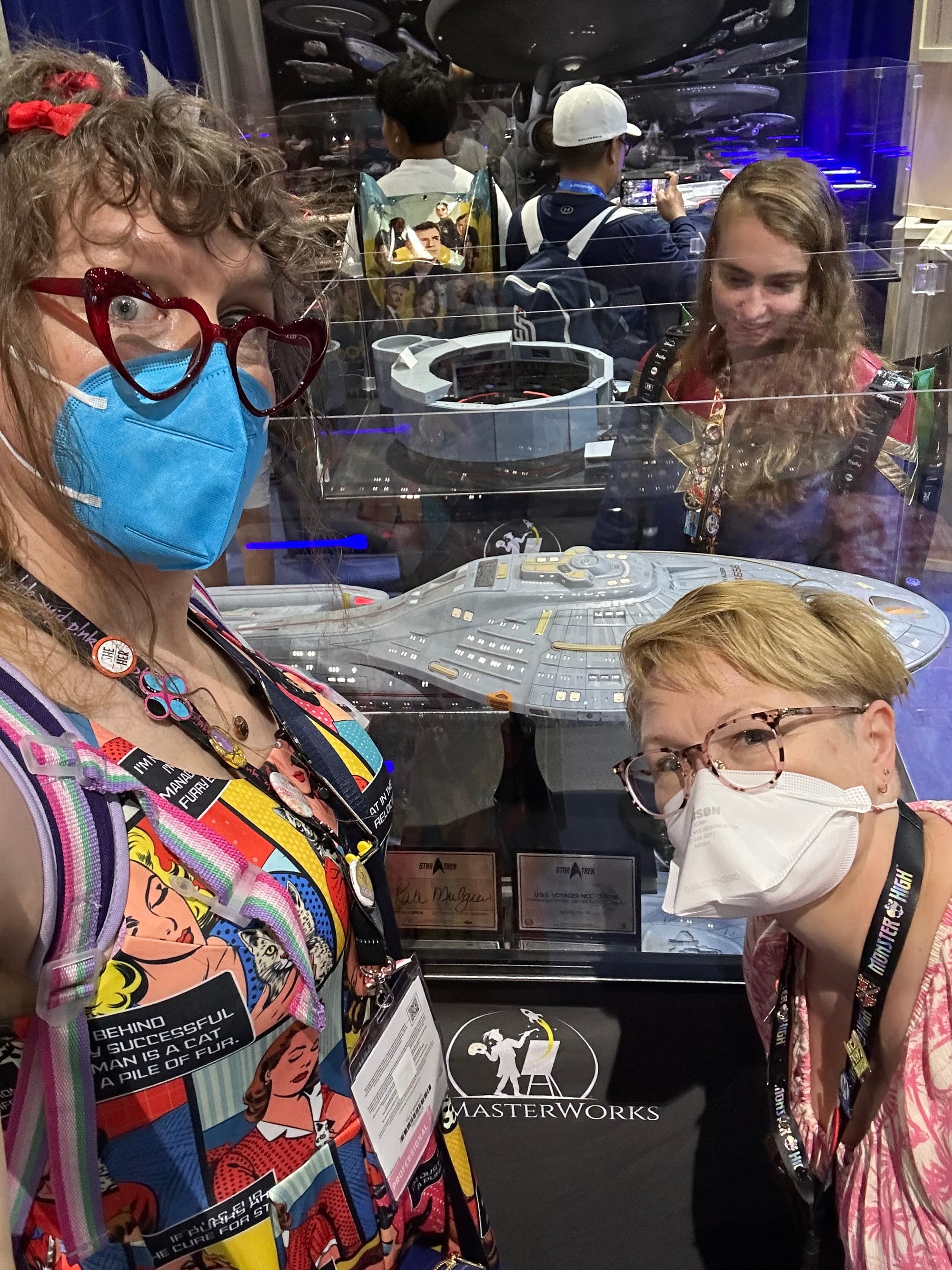 Tilly and Susan (masked!) on the SDCC con floor in front of a display case with a huge lit up scale model of Voyager
