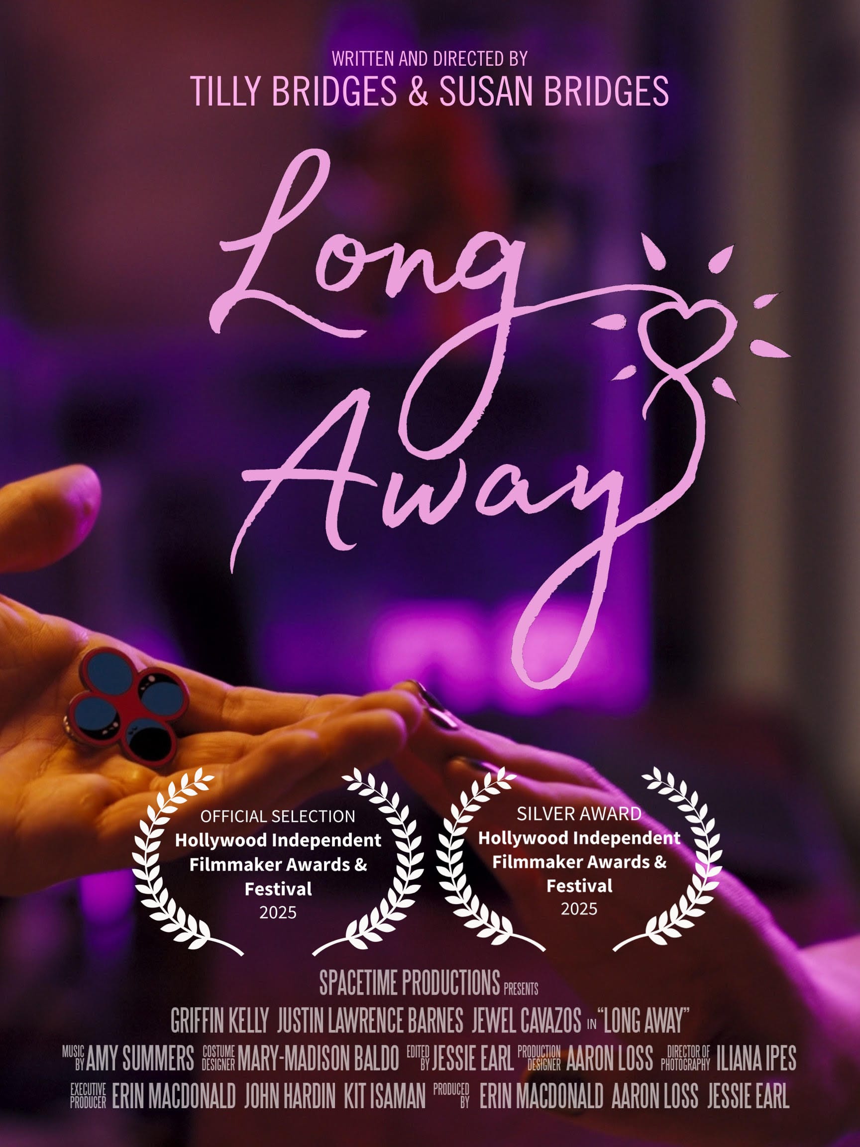 one hand reaching out, palm upward, holding an enamel pin displaying four circles, and another hand reaching out, palm downward, the two hands touch at the fingertips and are bathed in pink light. text reads: LONG AWAY WRITTEN AND DIRECTED BY TILLY BRIDGES & SUSAN BRIDGES SPACETIME PRODUCTIONS PRESENTS GRIFFIN KELLY JUSTIN LAWRENCE BARNES JEWEL CAVAZOS in “LONG AWAY” MUSIC BY AMY SUMMERS COSTUME DESIGN MARY-MADISON BALDO EDITED BY JESSIE EARL PRODUCTION DESIGNER AARON LOSS DIRECTOR OF PHOTOGRAPHY ILIANA IPES EXECUTIVE PRODUCER ERIN MACDONALD JOHN HARDIN KIT ISAMAN PRODUCED BY ERIN MACDONALD AARON LOSS JESSIE EARL official selection and silver award, hollywood independent filmmaker awards & festival 2025