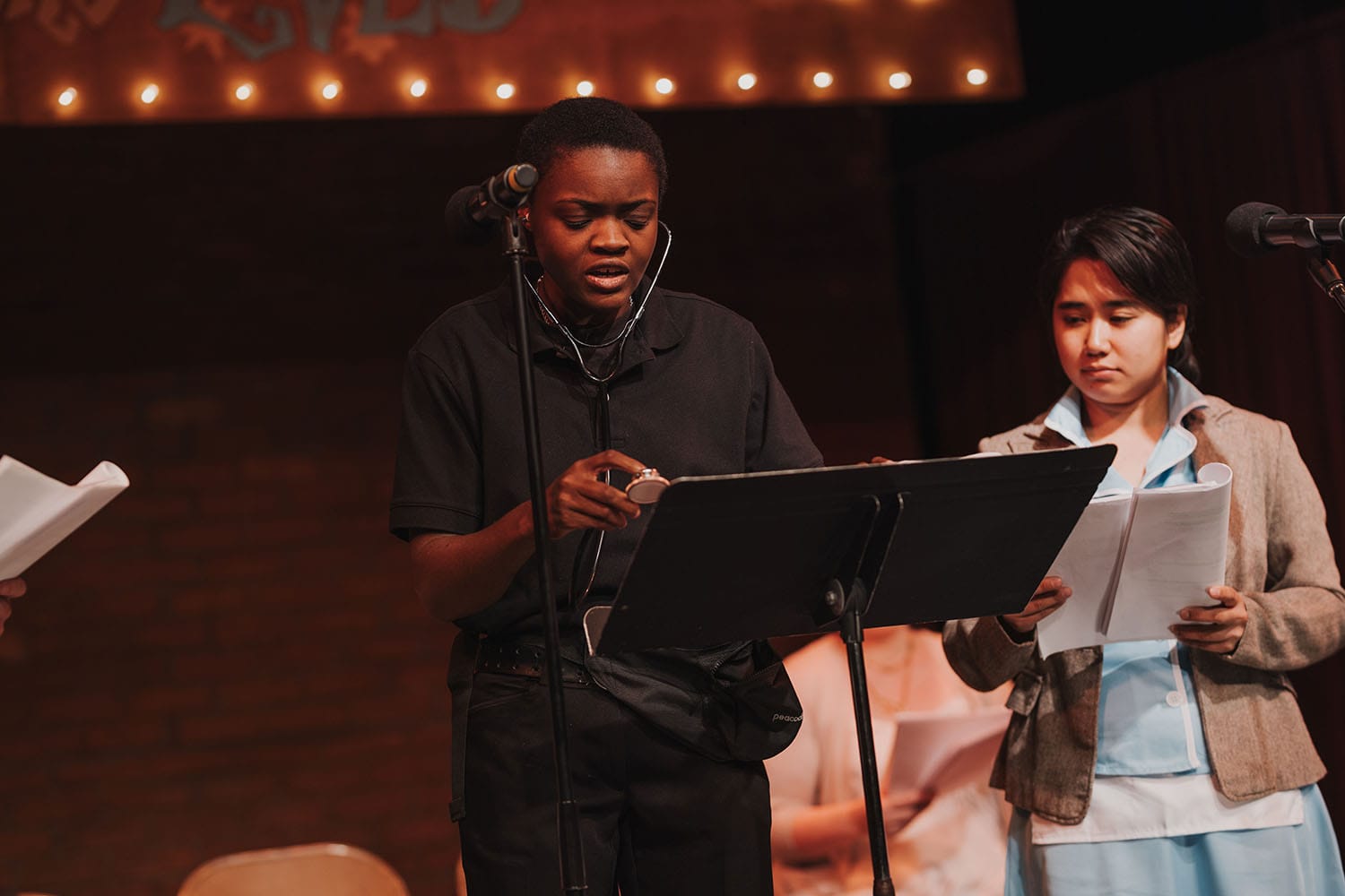 Olabisi Kovabel with a stethoscope next to Ari Villalon in a blazer over a waitress uniform