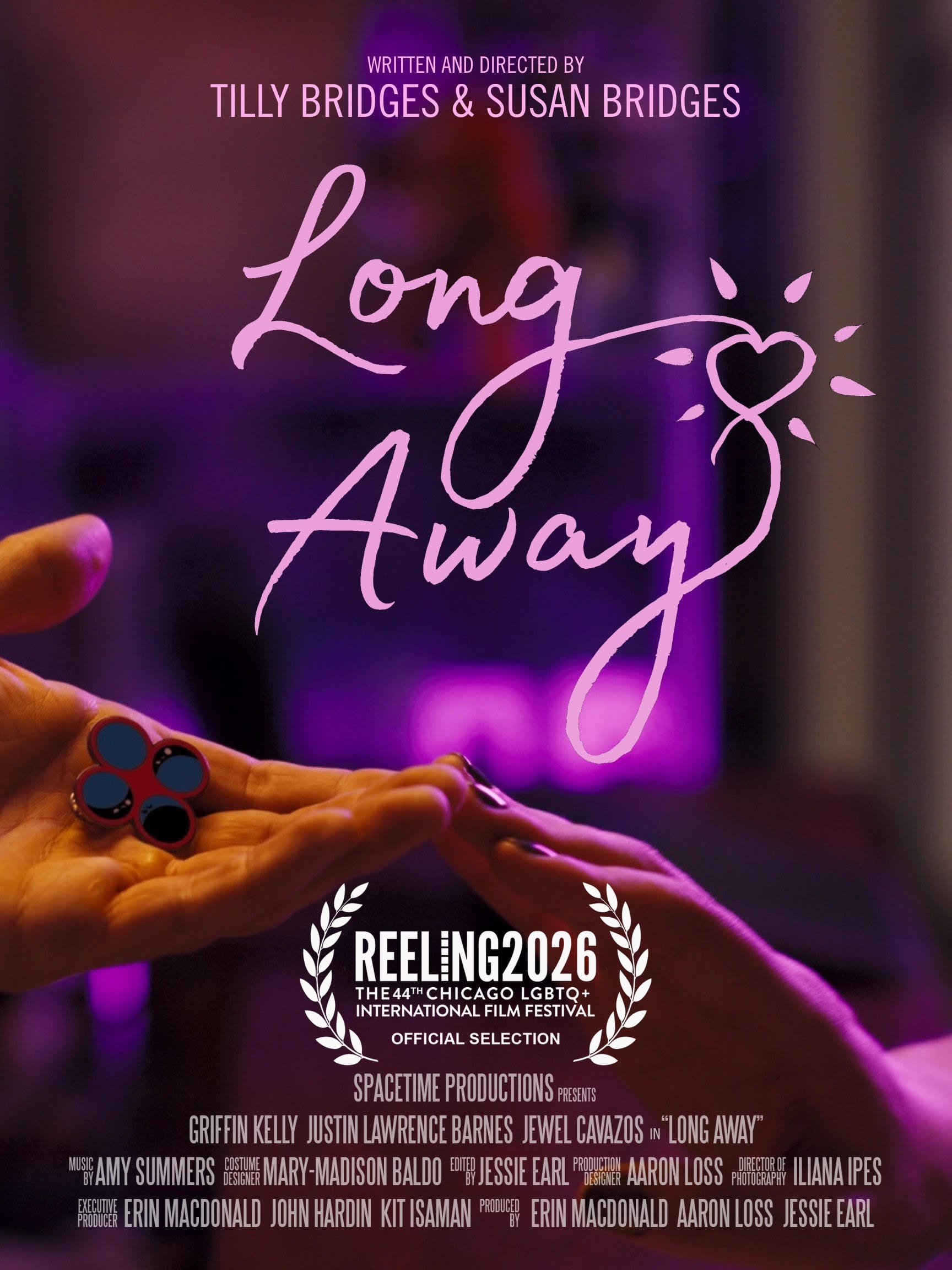 one hand reaching out, palm upward, holding an enamel pin displaying four circles, and another hand reaching out, palm downward, the two hands touch at the fingertips and are bathed in pink light. text reads: LONG AWAY WRITTEN AND DIRECTED BY TILLY BRIDGES & SUSAN BRIDGES SPACETIME PRODUCTIONS PRESENTS GRIFFIN KELLY JUSTIN LAWRENCE BARNES JEWEL CAVAZOS in “LONG AWAY” MUSIC BY AMY SUMMERS COSTUME DESIGN MARY-MADISON BALDO EDITED BY JESSIE EARL PRODUCTION DESIGNER AARON LOSS DIRECTOR OF PHOTOGRAPHY ILIANA IPES EXECUTIVE PRODUCER ERIN MACDONALD JOHN HARDIN KIT ISAMAN PRODUCED BY ERIN MACDONALD AARON LOSS JESSIE EARL Reeling 2026, the 44th Chicago LGBTQ+ International Fim Festival, Official Selection