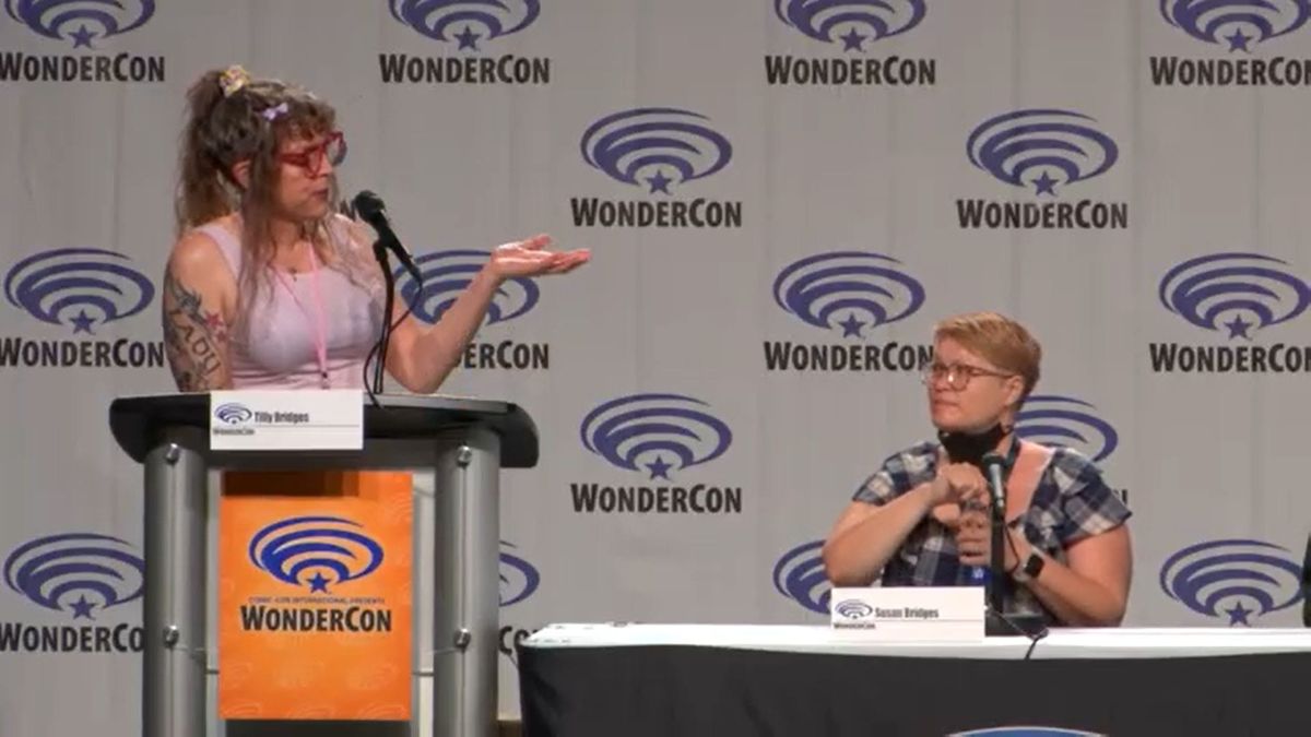 Tilly at a podium moderating, as Susan sits next to her at a table, from the WonderCon Long Away panel