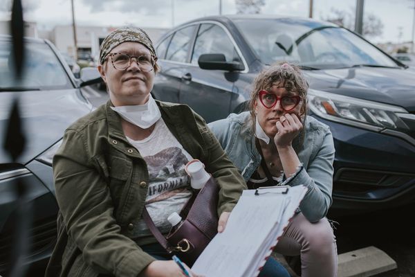 Tilly and Susan sitting down in a parking lot, looking up at the camera monitor during filming on “Long Away”