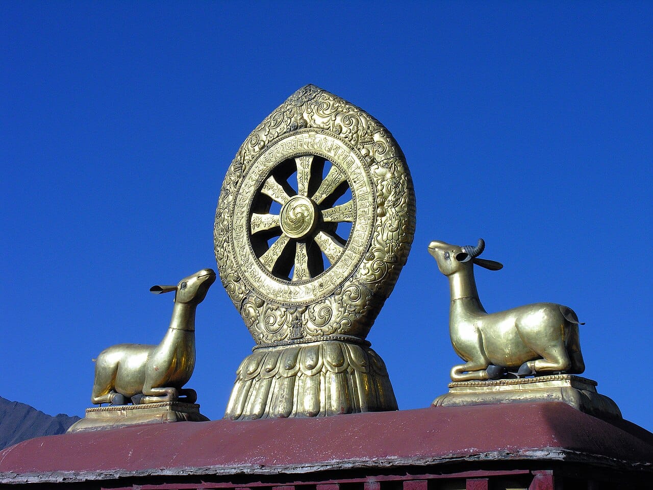 A large golden eight-spoked Dharma wheel flanked by golden deer.