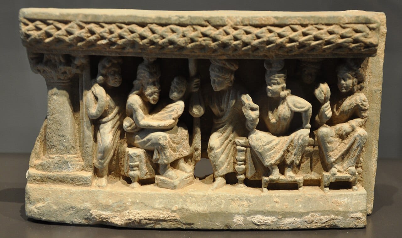 A slate relief of the seer Asita examining the baby Buddha, who is held by the king, surrounded by members of the court.