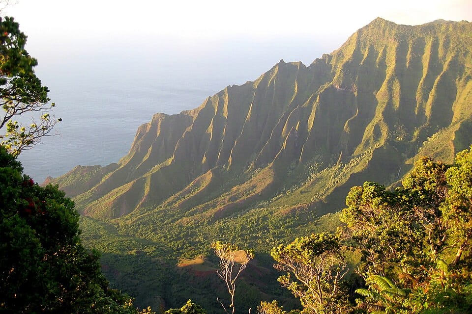 A beautiful, green valley in Hawaii, seen from high up, with the ocean in the background.