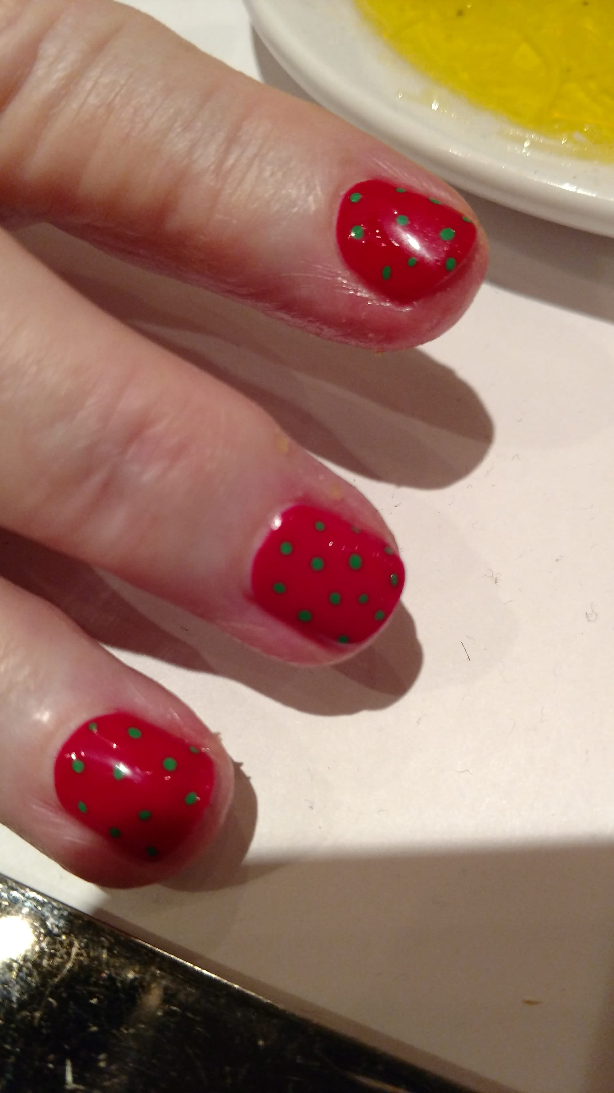 Close-up of a hand with bright red nails decorated with small green polka dots, holiday themed manicure.