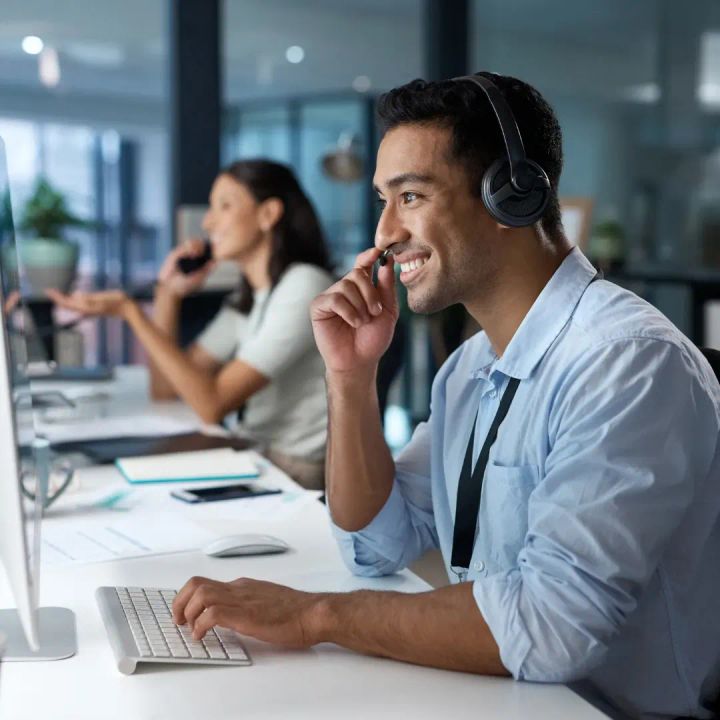 Customer service professionals wearing headsets work at computers in a modern office, representing AI-assisted support, communication, and human-centered customer experience.