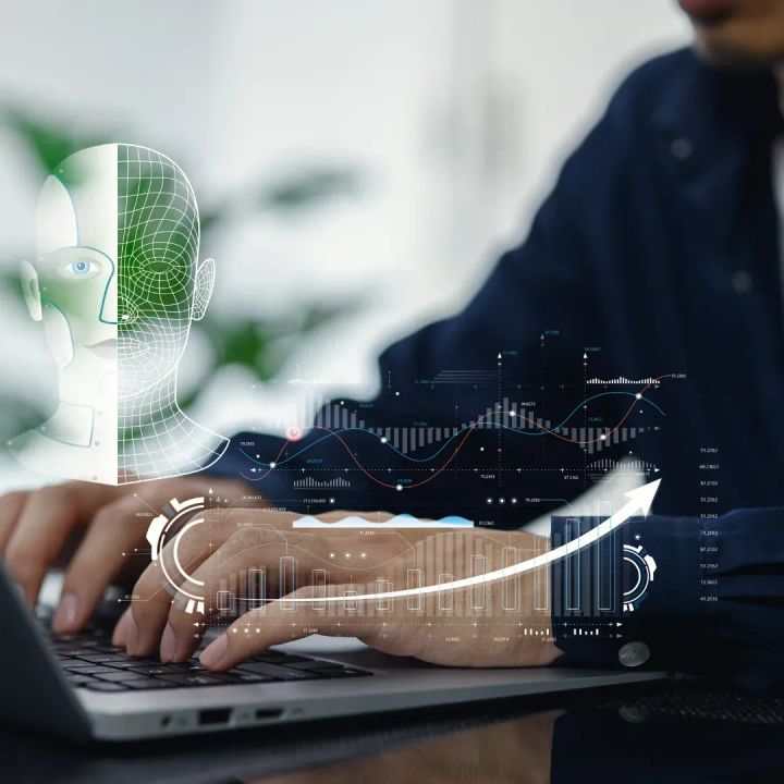 Business professional typing on a laptop with digital AI interface, charts, and a humanoid face overlay, representing AI strategy, data analysis, and human–technology collaboration.