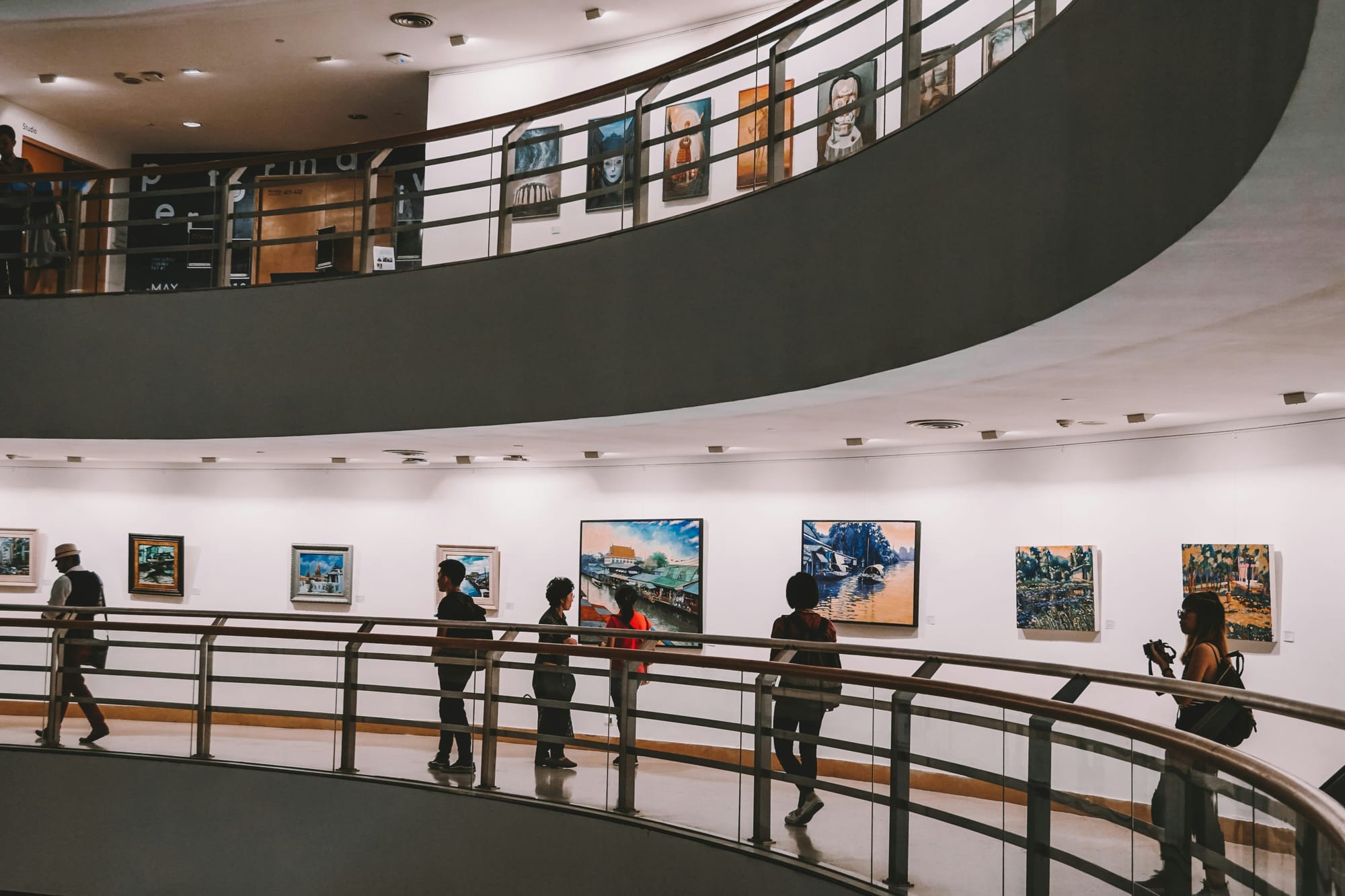 Visitors walking through a multi-level gallery space with colourful artworks on display