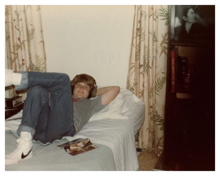 A 14-year-old Merlin lies on his bed, listening to music on Radio Shack headphones. In a moment he'll return to his TV Guide.