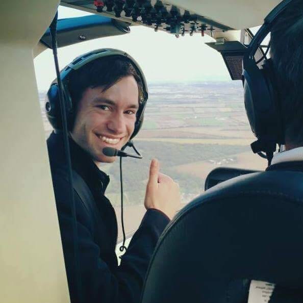 Dorian Rammer in die Kamera lachend, mit Daumen nach oben, im Cockpit eines Helikopters (im Flug)