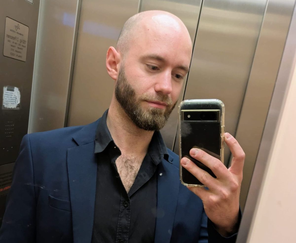 Spiegel-Selfie des Autors im Aufzug: Mann in blauem Sakko und schwarzem Hemd hält ein Smartphone.