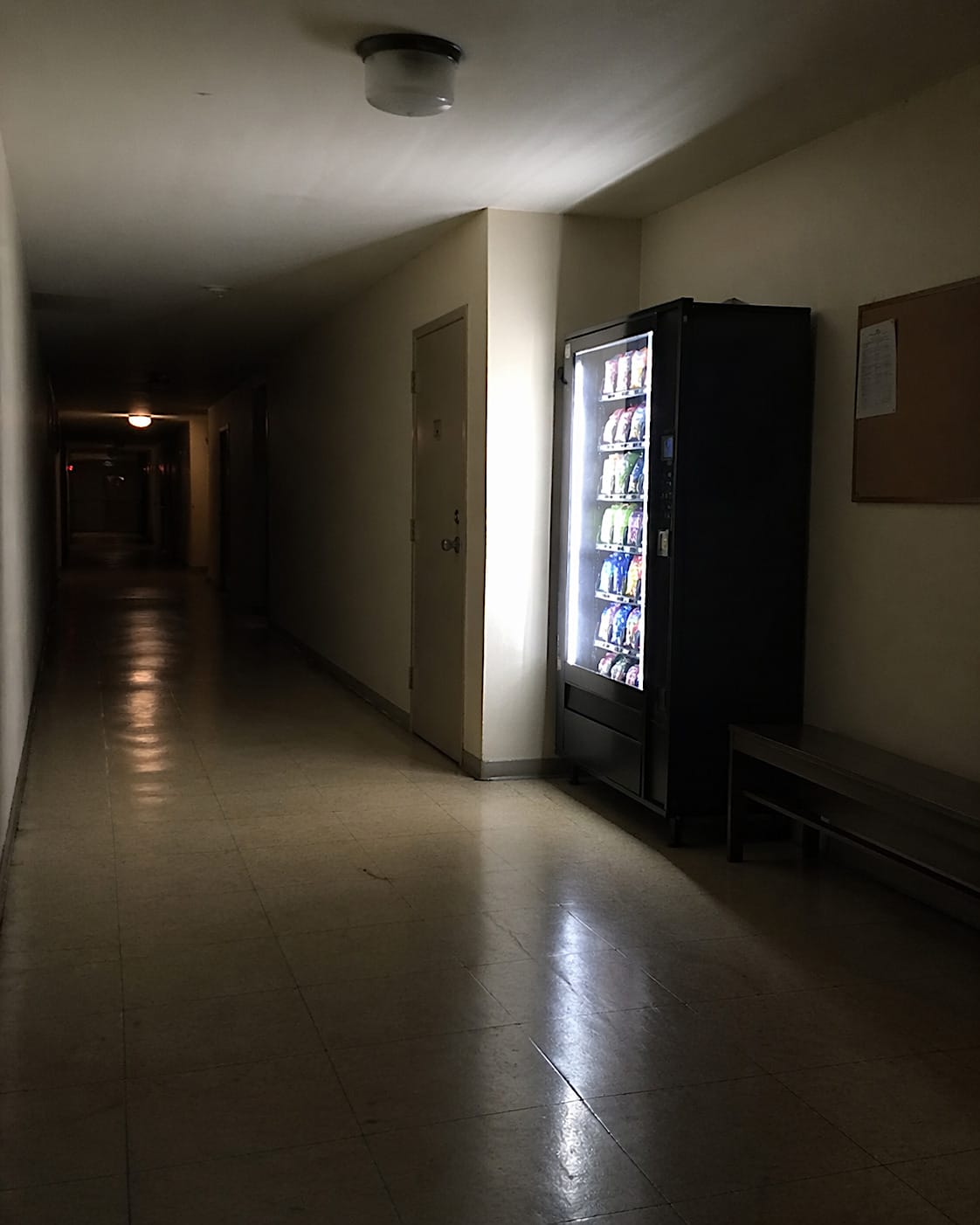 Glowing vending machine in a dim, mostly empty institutional corridor at night.