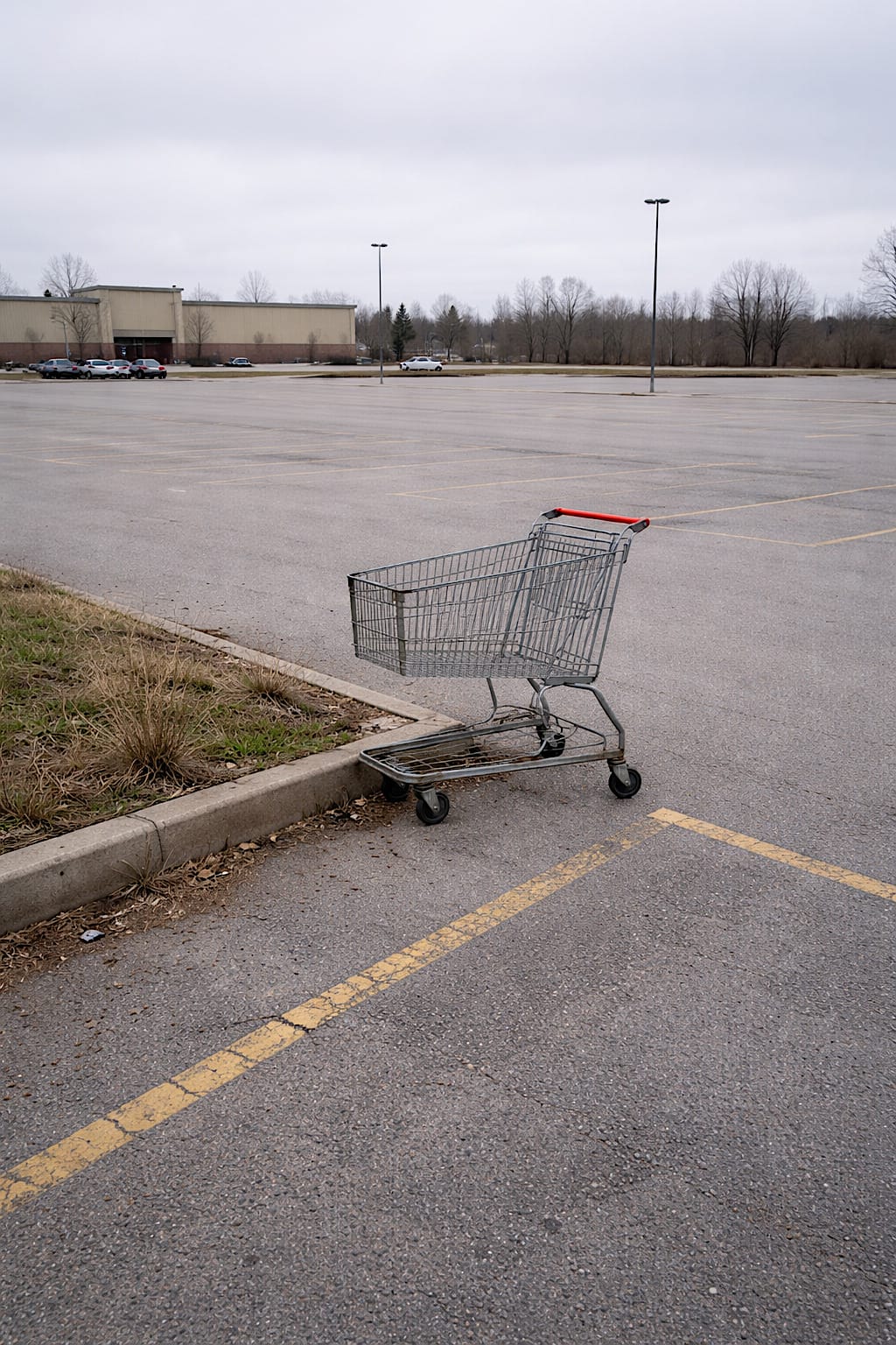 Single metal shopping cart sitting alone at the far edge of an empty parking lot.