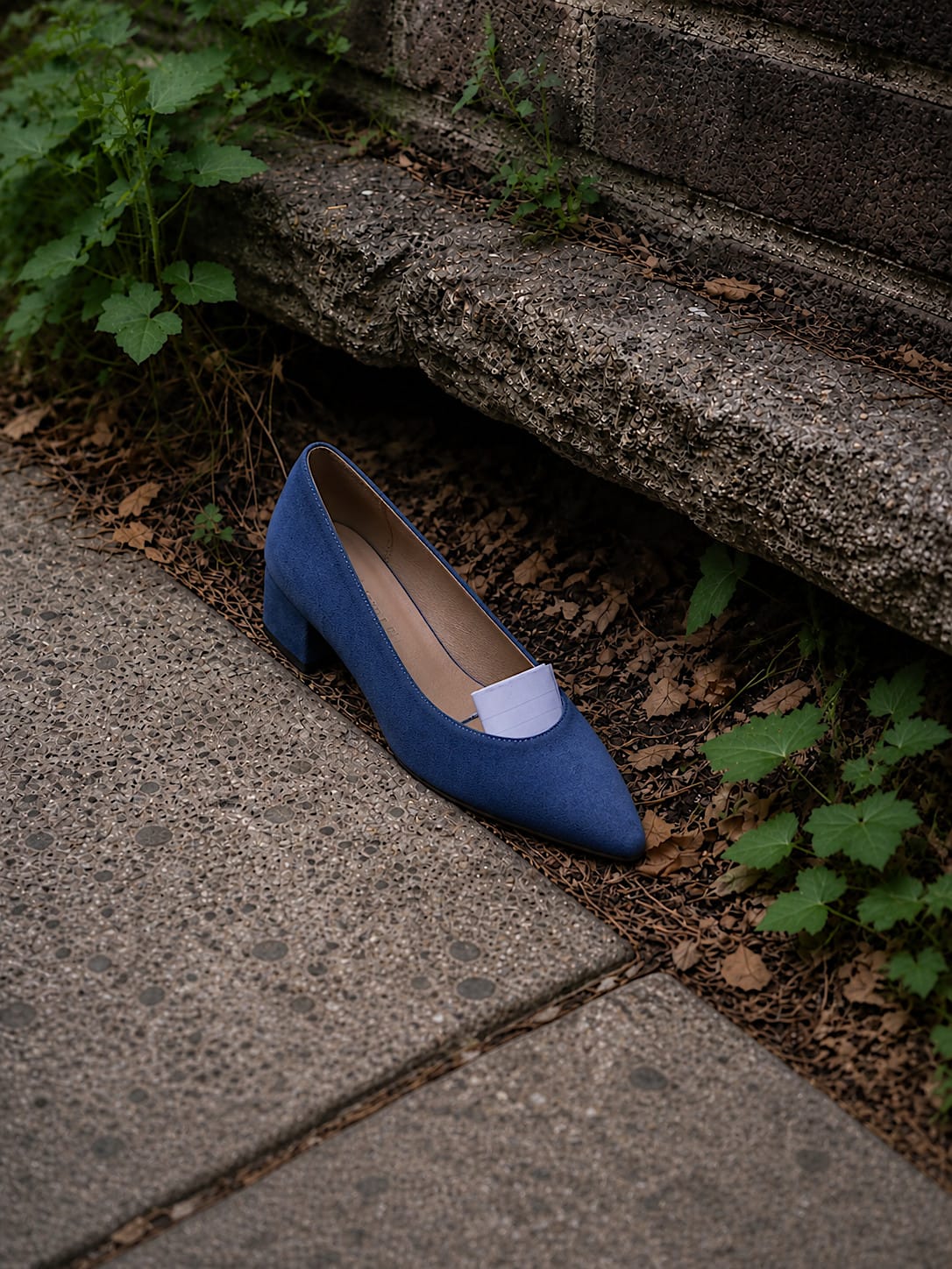 Women’s blue suede shoe on a sidewalk with a folded note tucked inside.