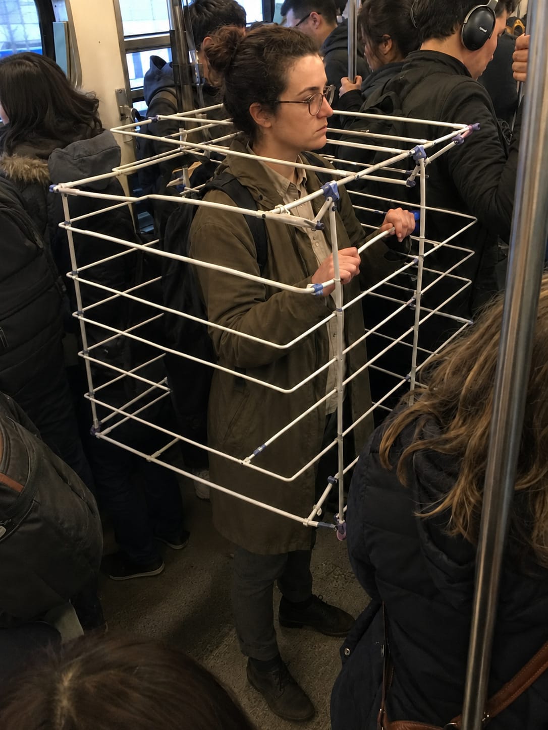 A packed commuter train passenger wears an open laundry drying rack as a personal-space barrier.
